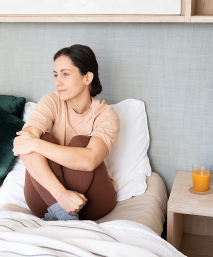 Frau sitzt mit nachdenklichem Blick auf Bett