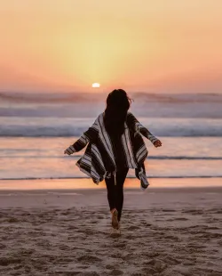Frau läuft am Strand in Richtung Sonnenuntergang