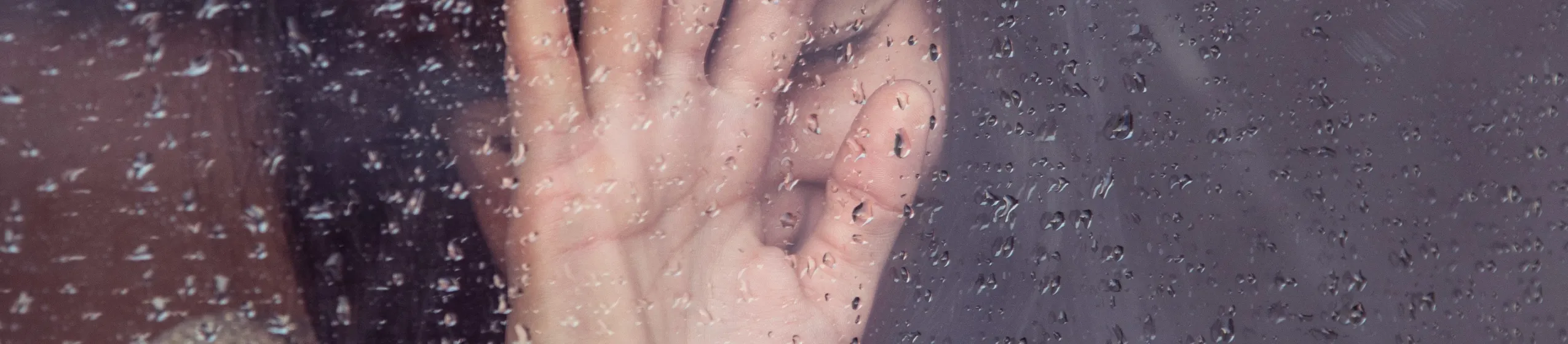 Frau drückt Hand gegen ein regennasses Fenster