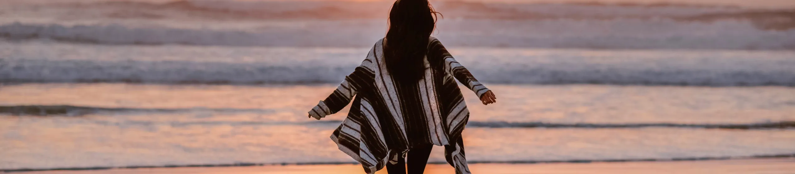 Frau läuft am Strand in Richtung Sonnenuntergang