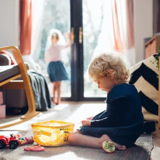 Ein Kind spielt am Boden, eines steht bei der Balkontür