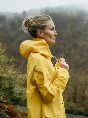Frau mit gelbem Regenmantel im Herbst