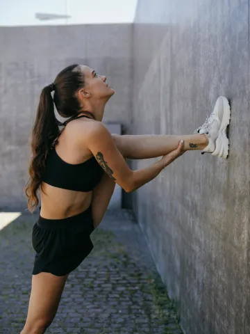 Frau dehnt ihr Bein an einer Wand