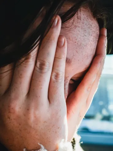 Frau mit Sommersprossen hält sich die Hände vor das Gesicht