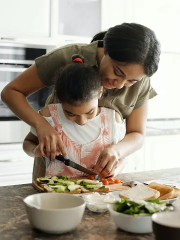 Kind schneidet mit der Mutter Gemüse in der Küche