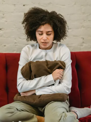 Frau sitzt überlastet, verheult und einen Polster umarmend auf einer Cuch