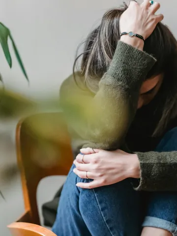 Frau hält sich müde und verzweifelt den Kopf und stützt sich beim Knie ab