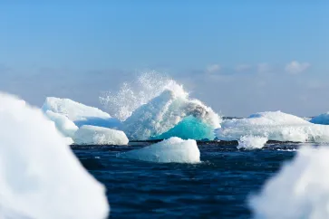 Eisberge im Meer an denen sich eine Welle bricht