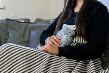 Frau mit Wärmeflasche sitzt auf dem Sofa