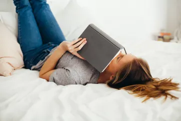 Frau mit Buch liegt auf Bett