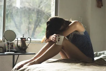 Frau ist sitzend nach vorne gebeugt mit Tasse in der Hand