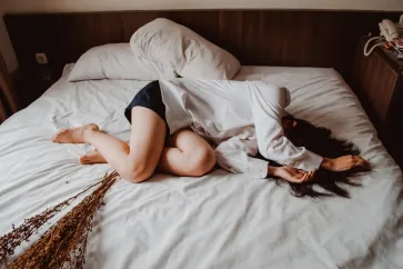 Frau liegt zusammengekauert auf dem Bett