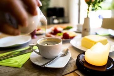 Kaffeetasse auf Tisch, in die Milch eingegossen wird