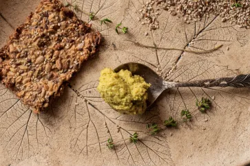 Zucchini Apfel Aufstrich auf einem Löffel und ein Sonnenblumenkernbrot