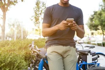 Mann mit Handy lehnt an Fahrrad