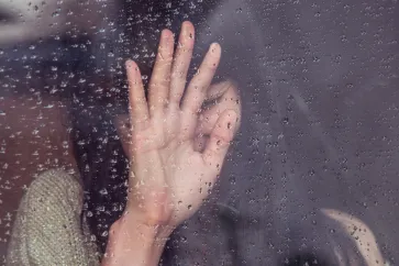 Frau drückt Hand gegen ein regennasses Fenster