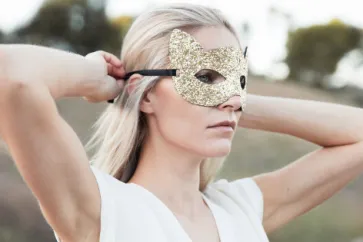 Frau bindet sich goldene Augenmaske um