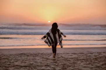 Frau läuft am Strand in Richtung Sonnenuntergang