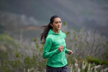 Frau im grünen Pullover läuft in den Bergen