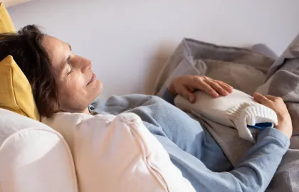 Frau liegt mit einer Wärmeflasche zugedeckt auf dem Sofa