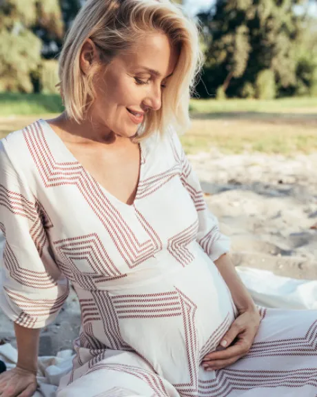 schwangere Frau sitzt in einem Kleid auf einer Decke im Freien