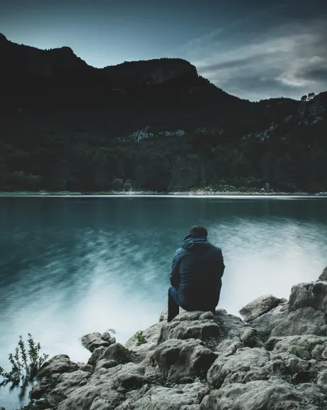 Mann, der in den Bergen auf einem Felsen vor einem See sitzt