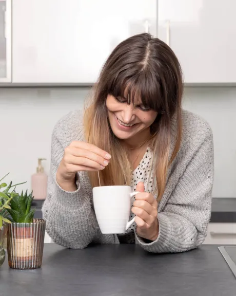 Frau steht mit einer Tasse Tee in der Küche