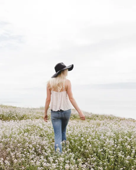 Frau mit Hut geht über Blumenwiese