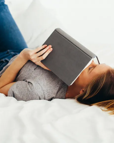 Frau mit Buch liegt auf Bett