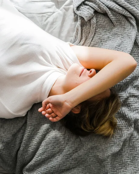 Frau liegt mit Arm über dem Gesicht im Bett