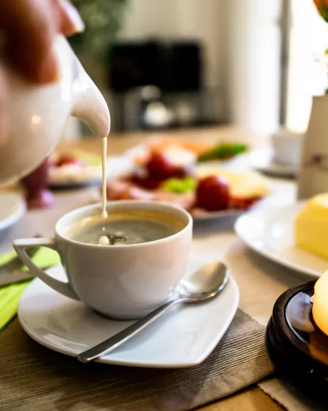 Kaffeetasse auf Tisch, in die Milch eingegossen wird