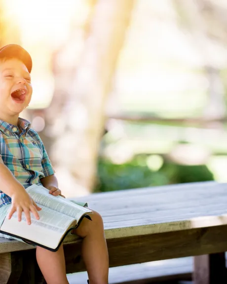 Kind mit Buch sitzt lachend in der Sonne