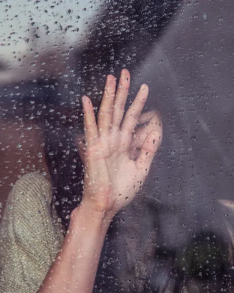 Frau drückt Hand gegen ein regennasses Fenster