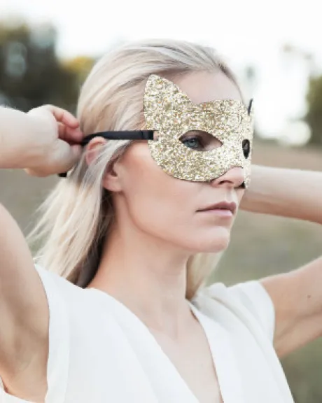 Frau bindet sich goldene Augenmaske um