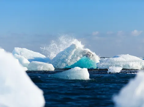 Eisberge im Meer an denen sich eine Welle bricht