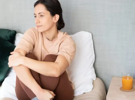 Frau sitzt mit gedankenverlorenen Blick auf Bett