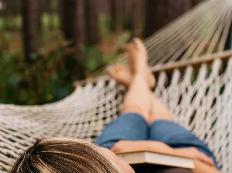 Frau liegt mit Buch in der Hängematte