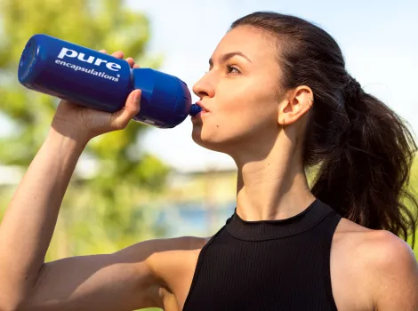 Frau trinkt aus einer Pure Encapsulations Trinkflasche