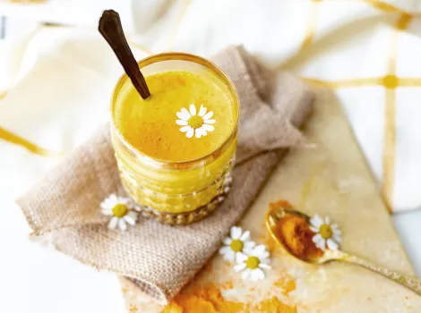 Ein Glas mit Curcuma-Latte und einem Löffel