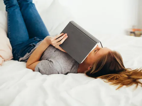 Frau mit Buch liegt auf Bett