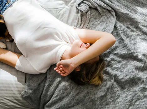 Frau liegt mit Arm über dem Gesicht im Bett