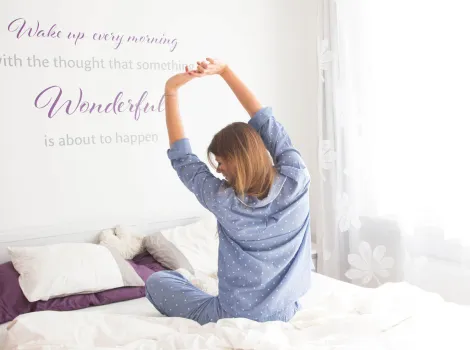 Frau sitzt im Bett und streckt sich