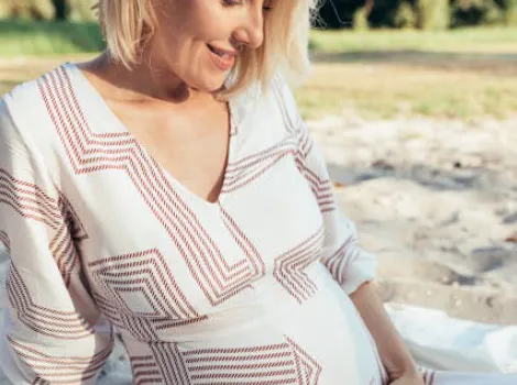 Schwangere Frau, in hellem Sommerkeid, die ihren Babybauch berührt