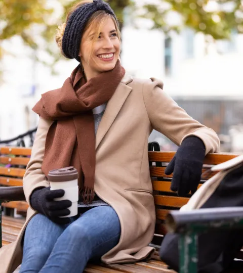 Immunsystem urban Frau braun Herbst Schal Kaffeebecher Handschuhe Rucksack lächeln Parkbank