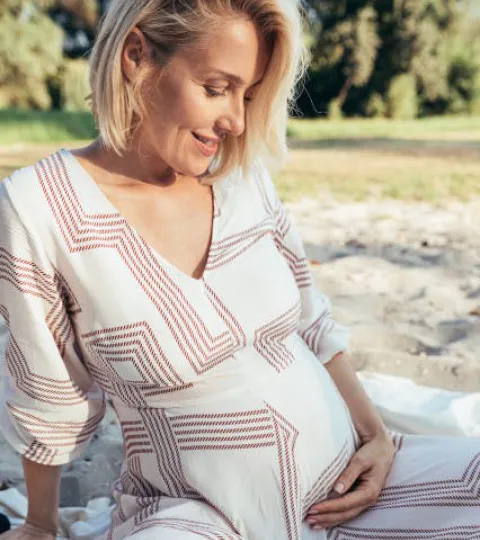 Schwangere Frau, in hellem Sommerkeid, die ihren Babybauch berührt