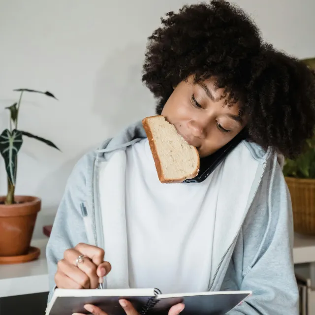 Frau hat ein Brot im Mund notiert konzentriert etwas