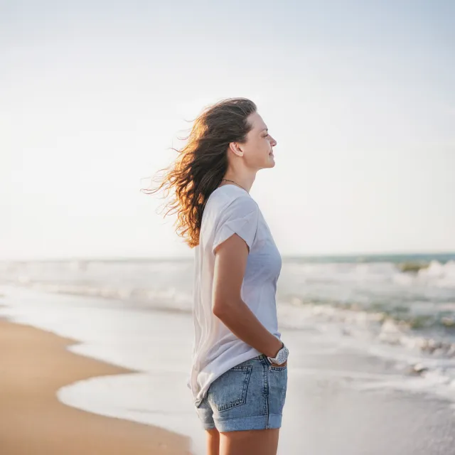 Frau steht lächelnd am Strand im Wind