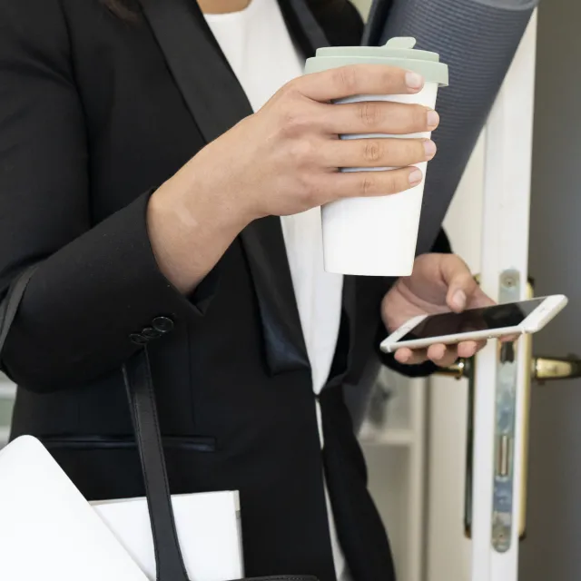Business-Frau mit Coffee-to-go, Yogamatte und Handy in der Hand