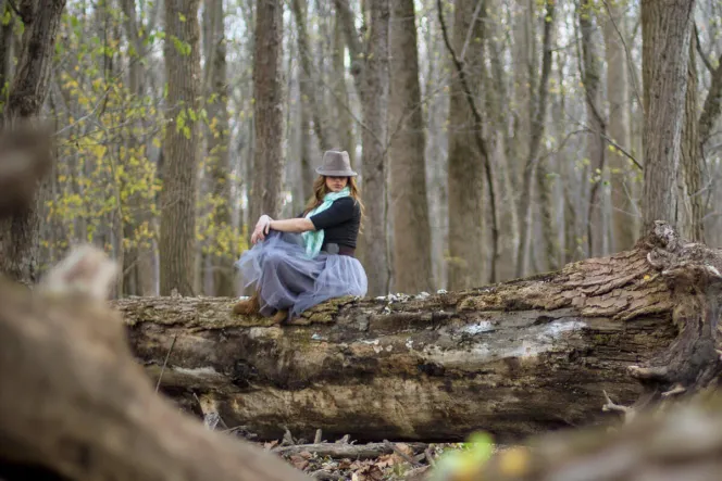 Frau mit Hut sitzt im Wald auf Baumstamm