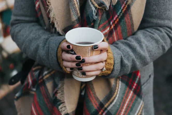 Frau mit dunklem Nagellack hält Kaffeebecher mit zwei Händen